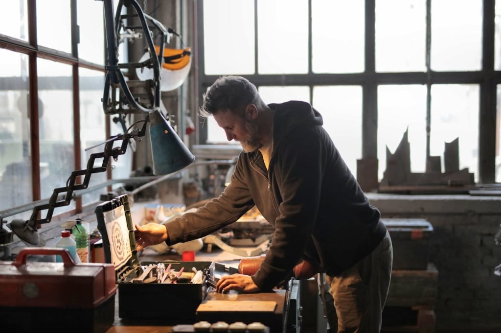 Servicios. A male craftsman focuses on his work in a sunlit industrial workshop, using tools from a nearby toolbox.